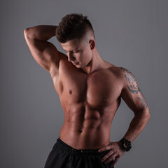 Fototapeta premium Fashionable sporty bodybuilder man model with hairstyle with sexy muscular body stands and poses in the dark on a gray background. Healthy lifestyle and diet