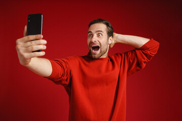 Young man expressing surprise while taking selfie on cellphone