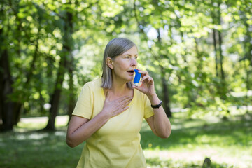 Senior retired woman with asthma breathing in an inhaler in a summer park