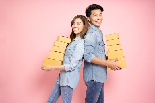 Asian couple holding package parcel box isolated on pink background, Delivery courier and shipping service concept
