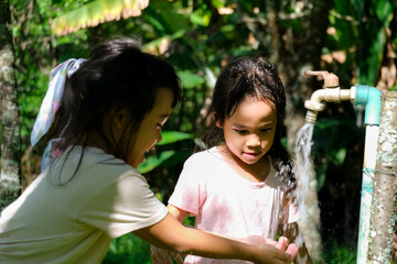 Two little sisters washing their hands at the outdoor faucet. Two cute girls turn on the faucet to...