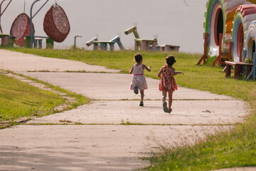 Obraz premium Rear view of children running on the road in the park. Two cute sisters are playing in the summer garden. Happy childhood concept.