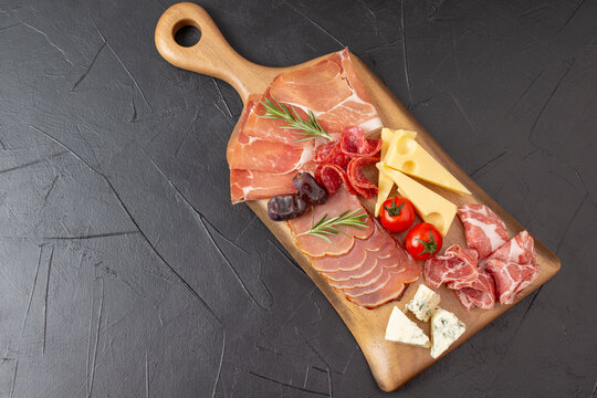 Mixed delicatessen with charcuterie and cheese board with a place for text. Italian appetizers or antipasto set with gourmet food on dark table
