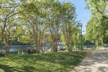 In the park along the Po river, people, friends and families enjoy the afternoon on a warm spring day. Two hammocks can be seen hanging from the trees. Turin, Italy. May 1, 2022.