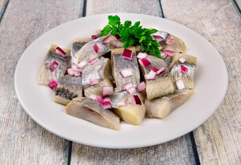 Mediterranean herring fillet served on a plate with chopped onion rings and parsley on the table