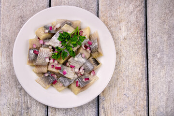 Mediterranean herring fillet served on a plate with chopped onion rings and parsley on the table
