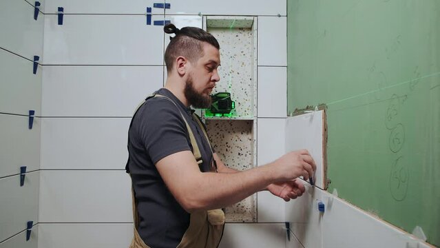 Tiler using tile leveling system when laying ceramic tiles on bathroom wall