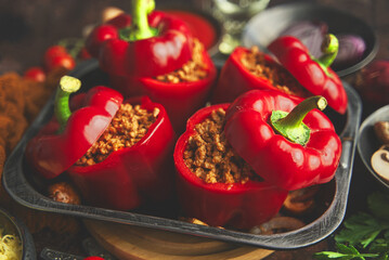 Red bell stuffed paprika peppers in iron cooking pot with various ingredients on side