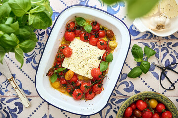 trendy vegan health food. feta cheese with small cherry tomatoes in olive oil with herbs and spices in a enamel baking dish. vegan menu. simple cheese dishes. top view, selective focus