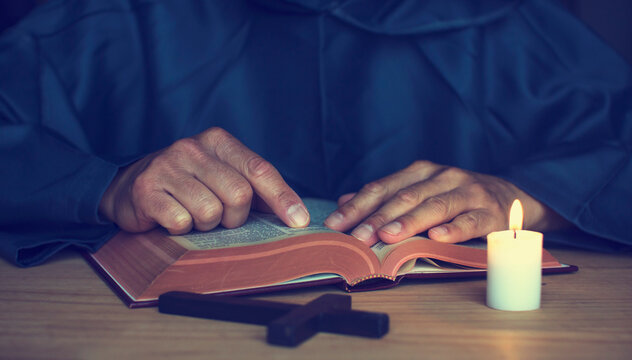Vintage image of a monk reading a book in the dark under the light of a lit candle.