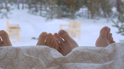 Close-up of toes under a blanket, male and female legs in the bed of a country house overlooking...