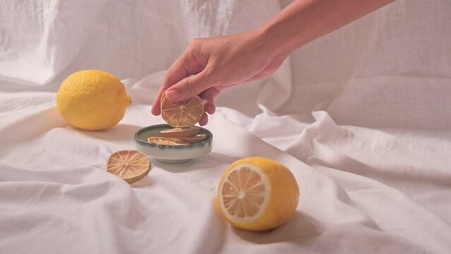 Hand putting dried lemon slices on a ceramic platter for making tea showing health, wellness and spring aesthetic