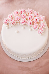 Gorgeous beige birthday cake with pink flowers on the table.