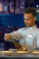 Portrait of african young bartender man opens a bottle of whiskey. Concept of service