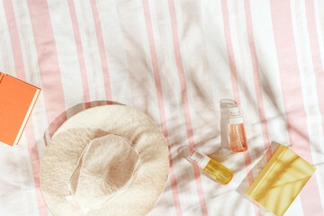 Summer pastel background with wide-brimmed sun hat, cosmetics products, book on striped beach towel...