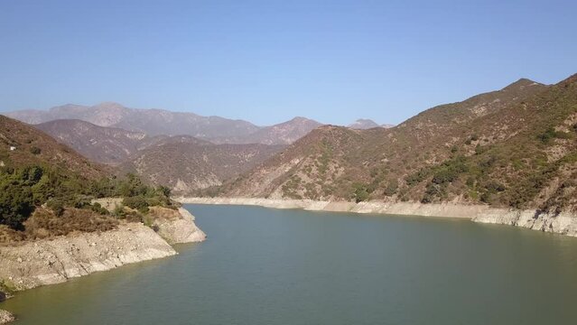 stunning aerial footage of the vast rippling waters of Morris Reservoir surrounded by majestic mountain ranges covered in lush green trees and plants with blue sky at Azusa Wilderness Park in Azusa 