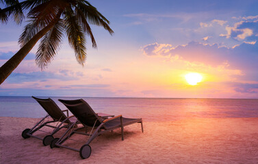 art sunset over Tropical paradise beach with a sun-lounger facing the blue sea - obrazy, fototapety, plakaty