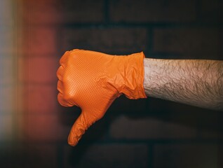 The hand of a young man in a rubber glove on an isolated background of a brick wall in close-up,...