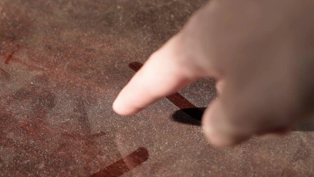 The finger draws a cross on the dust close-up. Mark a place for urgent cleaning. Dusty old sideboard