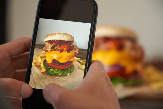 unrecognizable man taking a picture of a delicious burger with his phone.