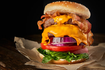 Close-up of home made tasty burger with onion, lettuce, cheddar cheese, bacon and tomato on a...