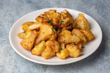 Fried in batter Cauliflower florets served on a black plate on a grey concrete table with ingredients, view from above, close-up, flatlay, copy space