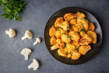Fried in batter Cauliflower florets served on a black plate on a grey concrete table with ingredients, view from above, close-up, flatlay, copy space