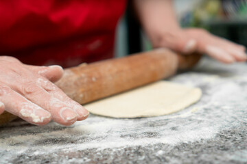 Close-up of women's hands rolling out a wooden rolling pin yeast dough for croissants on the table sprinkled with flour