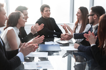 Business people sitting at the table while two of them shaking h
