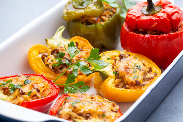 Stuffed peppers, halves of peppers stuffed with rice, dried tomatoes, herbs and cheese in a baking dish on a blue wooden table, top view. (Turkish name; biber dolmasi)