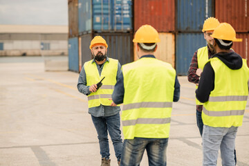 Obraz na płótnie Canvas Port workers in a yellow helmet in an industrial shipyard, arguing with their colleagues and controlling container transportation and export with commercial docks.