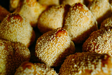 close-up of a bun with sesame seeds, lots of fresh baked goods