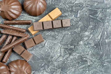 Slices of bitter, dark and milk chocolate, marmalade and marshmallows in chocolate cocoa glaze close-up on a black background. Space for text.