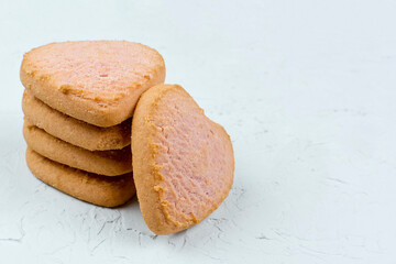 Heart-shaped cookies are stacked on top of each other on a gray (light) background. Space for the text. List of ingredients, recipe. The concept of the holiday.