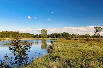 Beneath a blue sky on a summer day in Wisconsin, the Ahnapee State Trail passes its namesake river, reflecting the surrounding landscape of forests and marshes.
