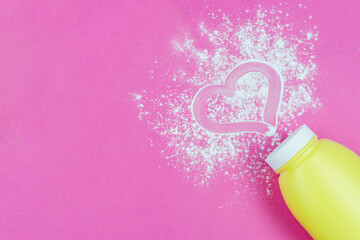 Scattered children powder under a diaper from a yellow bottle on a bright pink background. A drawing of a heart made with a finger on the powder. Space for the text. Love for your baby.