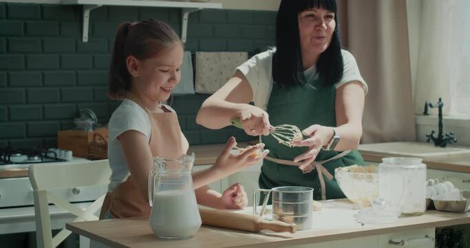 Happy family mom and kid daughter kneading dough baking pastry. Young girl helping mother on kitchen.