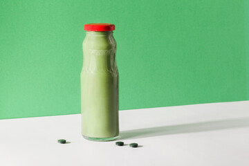 green smoothie in bottle and spirulina algae pills on green and white background. useful habits, self care and healthy lifestyle concept. quick snack
