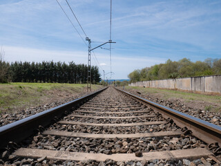 View from the train tracks towards an infinite straight between sleepers and the ballast under the wires of the catenary