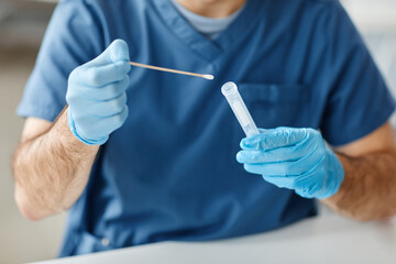 Unrecognizable medical worker wearing protective latex gloves taking out stick from tube to do swab...