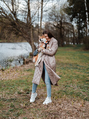 Fototapeta premium Young millennial beautiful woman brunette is walking with her Japanese breed shiba inu dog outdoor near the riverside bank on a leash. 