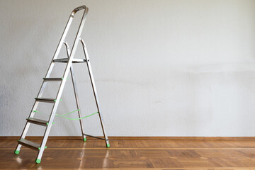 Foldable chrome stepladder against blank wall indoors