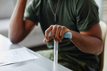 Unrecognizable young Black man in military uniform with walking stick sitting at table in psychotherapist office