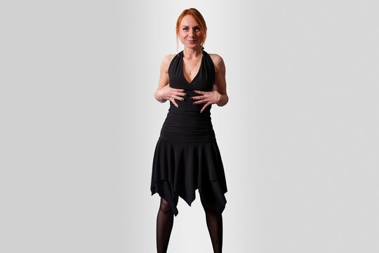Girl in a black dress playfully supports her breasts, on a gray background