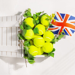 Tennis competition in the Great Britain. Sport composition with yellow tennis balls in a wooden box with green branches and the flag of Great Britain on a white background. Flat lay
