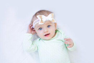 portrait of a happy and smiling little baby girl in a crib on a white isolated empty background or a cotton bed with a bow on her head with blue eyes and a green bodysuit