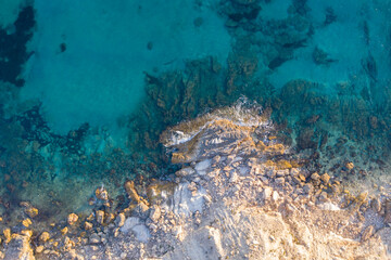 Aerial top down view of waves crashing against rocks in turquoise sea water