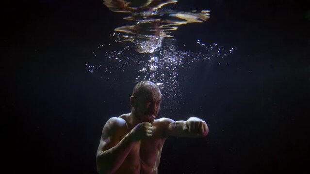 a man with a bare torso is boxing in dark water with bubbles and is reflected in the surface. three-quarter view