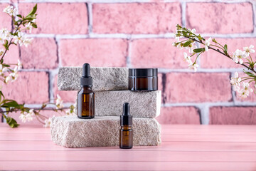 bottles for cosmetics on the podium made of stone and branches of cherry blossoms on a pink...