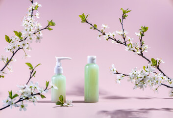 containers for cosmetics and branches of cherry blossoms on a pink background